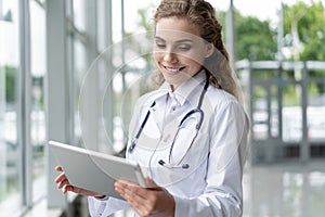 Healthcare, technology and medicine concept - smiling female doctor with stethoscope taking notes at tablet pc computer.
