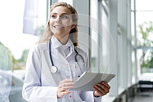 Healthcare, technology and medicine concept - smiling female doctor with stethoscope taking notes at tablet pc computer.