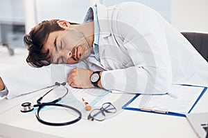 Healthcare, tired and a doctor man sleeping at his desk in the hospital with fatigue or exhaustion. Medical, burnout and