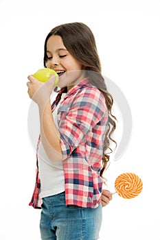 Healthcare tricks. Kid girl cunning eats apple while holds lollipop behind back. Whom she tries to trick. Girl pretend