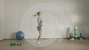 Healthcare and wellness advertisement concept. Athletic woman fitness coach doing classic skipping rope jumps, side view