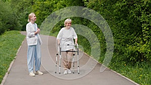 A healthcare worker accompanies an elderly woman as she walks with a walker.