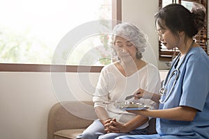 Healthcare worker or caregiver visiting senior woman indoors at home, explaining medicine dosage