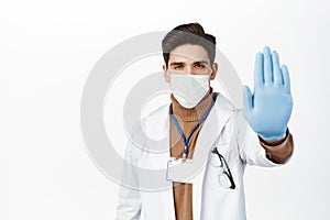 Healthcare worker in face mask from covid 19, wearing rubber gloves, showing stop no gesture, taboo and prohibition sign