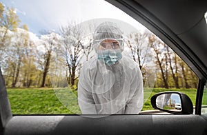 Healthcare worker in hazmat suit looking into car