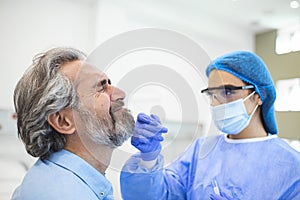 Healthcare worker with protective equipment performs coronavirus swab on elderly man. Nose swab for Covid-19