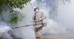 Healthcare worker using fogging machine spraying chemical to eliminate mosquitoes on overgrown at slum area