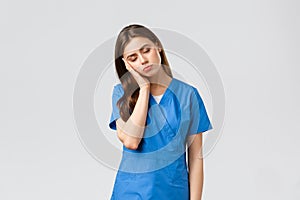 Healthcare workers, prevent virus and medicine concept. Tired sleepy female doctor, young nurse in blue scrubs, lean on