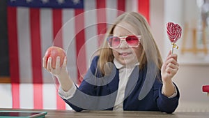 Healthful apple and unhealthy sweet lollipop in hands of blurred teenage schoolgirl choosing snack. Unsure teen girl