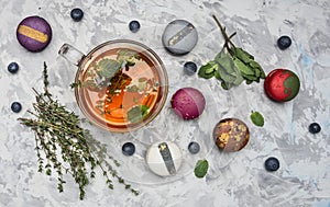 Healthful hot herbal tea with berries, thyme and mint, appetizing, multicolored macaroons on white rustic background, top view