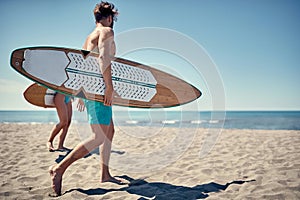 Healthy Active Lifestyle. Surfing. Summer Vacation. Extreme Sport. Young surfer man walking with board on the sandy beach. .