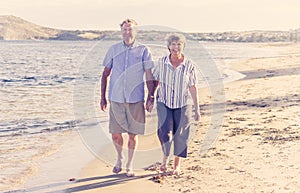 Healthy active senior couple holding hands, embracing each other and walking on beach