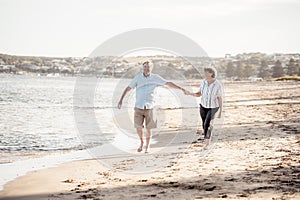 Healthy active senior couple holding hands, embracing each other and walking on beach