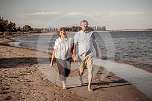 Healthy active senior couple holding hands, embracing each other and walking on beach