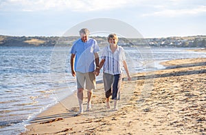 Healthy active senior couple holding hands, embracing each other and walking on beach