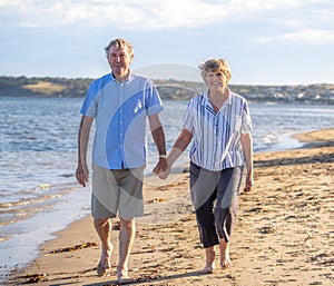 Healthy active senior couple holding hands, embracing each other and walking on beach