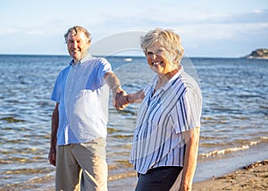 Healthy active senior couple holding hands, embracing each other and walking on beach