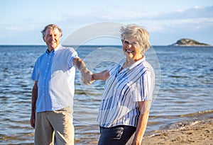 Healthy active senior couple holding hands, embracing each other and walking on beach