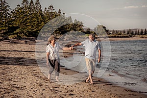 Healthy active senior couple holding hands, embracing each other and walking on beach