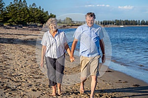 Healthy active senior couple holding hands, embracing each other and walking on beach