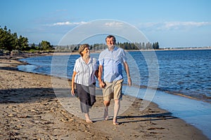 Healthy active senior couple holding hands, embracing each other and walking on beach