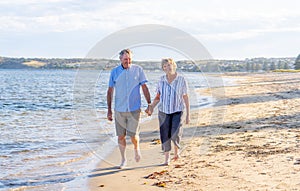 Healthy active senior couple holding hands, embracing each other and walking on beach