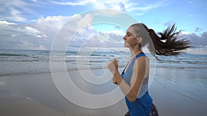 Healthy active woman in blue top running on the beach near sea on sunset.