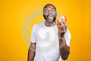 Healthy african american man holding an apple isolated against yellow background