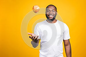 Healthy african american man holding an apple isolated against yellow background