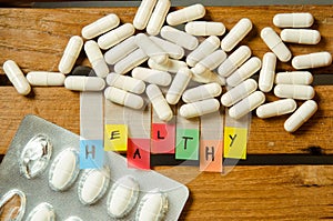 Healthy alphabet and capsule drug with medicine dose on wood background
