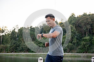 A healthy Asian man in sportswear is his calories burning on his smartwatch while running outdoors