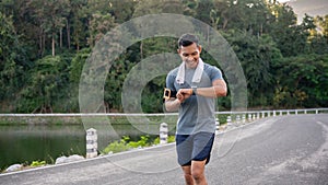 A healthy Asian man in sportswear is his calories burning on his smartwatch while running outdoors