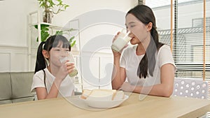A Healthy Asian mum and daughter drink fresh milk together at a dining table.