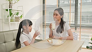 A Healthy Asian mum and daughter drink fresh milk together at a dining table.