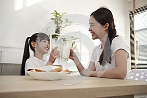 A Healthy Asian mum and daughter drink fresh milk together at a dining table