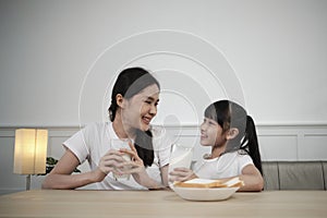 A Healthy Asian mum and daughter drink fresh milk together at a dining table