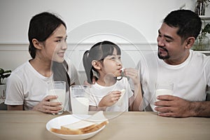 Healthy Asian parents and a daughter drink fresh milk together at dining table