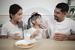 Healthy Asian parents and a daughter drink fresh milk together at dining table