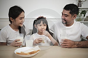 Healthy Asian parents and a daughter drink fresh milk together at dining table