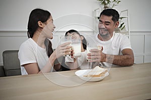 Healthy Asian parents and a daughter drink fresh milk together at dining table