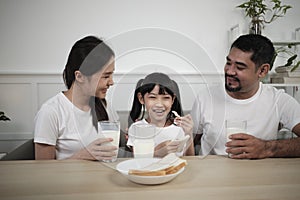 Healthy Asian parents and a daughter drink fresh milk together at dining table