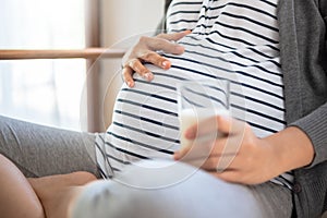 Healthy Asian Pregnant woman holding glass of milk and touching her belly at home