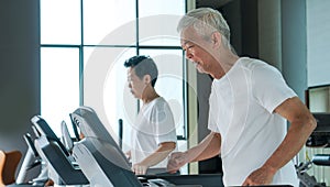 Healthy Asian senior couple exercise together in gym running treadmill