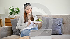 Healthy Asian woman eating her fresh and organic salad while relaxing in her living room