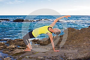 Healthy Asian woman practicing yoga at beach wearing yellow top