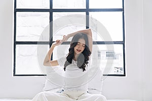 Healthy asian woman waking up relax muscles beside window early in morning. Happy young girl stretching raised arms muscles body
