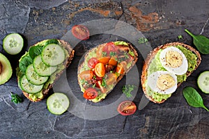 Healthy avocado toast assortment top view over a dark stone background