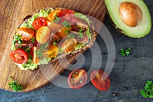 Healthy avocado toast with cherry tomatoes, close up table scene over a dark background