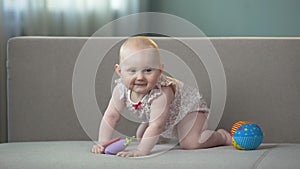 Healthy baby jumping on sofa, playing with colorful toys, enjoying happy life