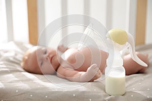 Healthy baby lying in cot, focus on breast pump with milk